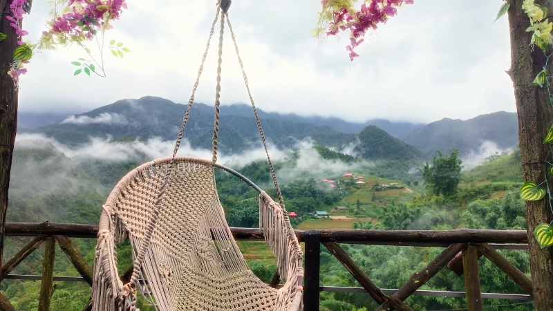Hanging chair on a balcony overlooks misty mountains and rice terraces in Sapa Vietnam